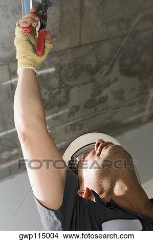 Low angle view of a male construction worker working with pliers View Large Photo Image Picture - Low angle view of a male construction worker working with pliers. Fotosearch