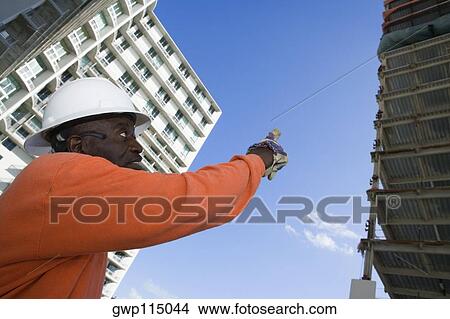 Picture - Low angle view of a male construction worker pointing towards the building. Fotosearch