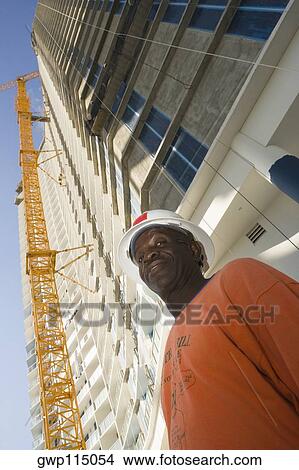 Low angle view of a male construction worker standing in front of a building View Large Photo Image Picture - Low angle view of a male construction worker standing in front of a building. Fotosearch