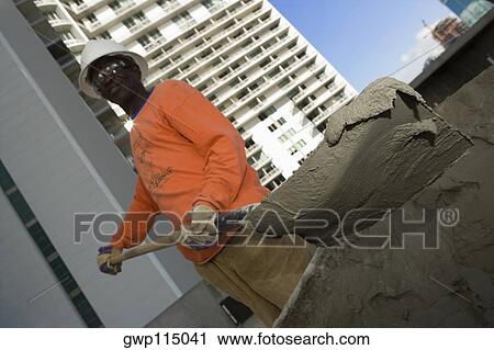 Stock Image - Low angle view of a male construction worker shoveling cement. Fotosearch