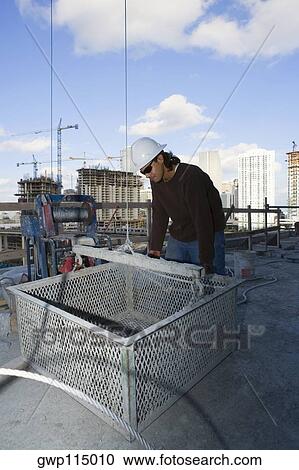 Stock Image - Male construction worker leaning against a basket at a construction site. Fotosearch