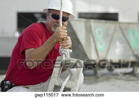 Male construction worker tightening a rope on a concrete block View Large Photo Image Stock Photo - Male construction worker tightening a rope on a concrete block. Fotosearch