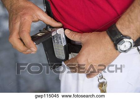 Stock Photography - Mid section view of a man fastening a mobile phone on his belt. Fotosearch