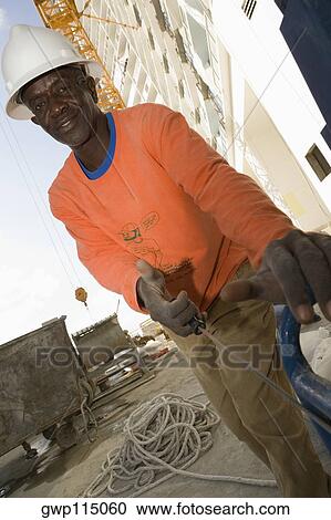 Stock Image - Portrait of a mid adult man pulling a generator cable at a construction site. Fotosearch