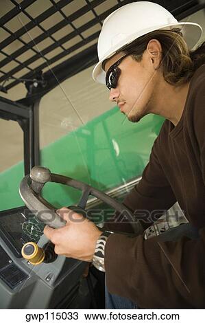 Stock Image - Side profile of a male construction worker operating a crane. Fotosearch