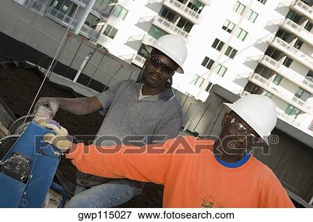 Two male construction workers working at a construction site View Large Photo Image Stock Photo - Two male construction workers working at a construction site. Fotosearch