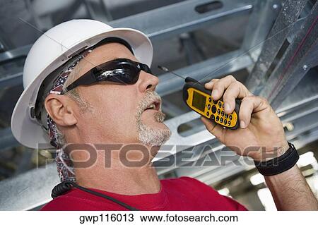 Stock Image - Close-up of a male construction worker talking on a walkie-talkie. Fotosearch