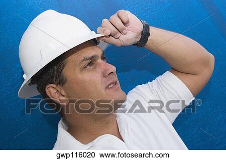 Stock Image - Close-up of a male construction worker adjusting his hardhat. Fotosearch