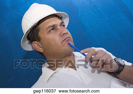 Stock Photo - Close-up of a male construction worker holding a pen and thinking. Fotosearch