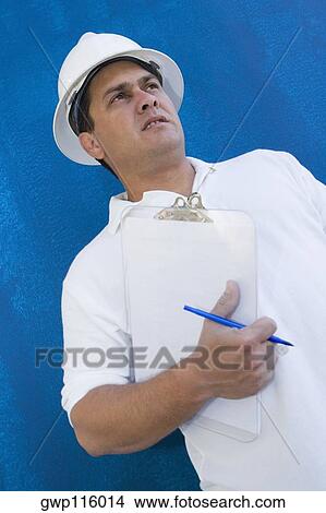 Picture - Low angle view of a male construction worker holding a clipboard and a pen. Fotosearch