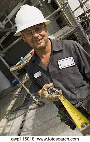 Stock Photo - Portrait of a male construction worker holding a tape measure and smiling. Fotosearch