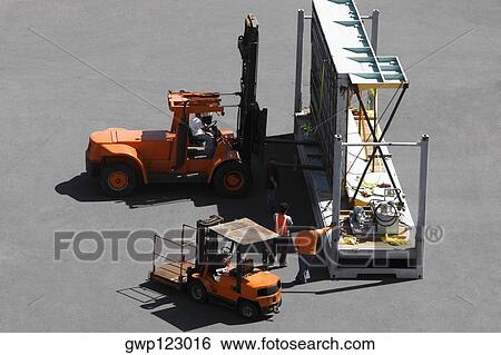 Stock Photograph - High angle view of forklifts and workers at a commercial dock. Fotosearch