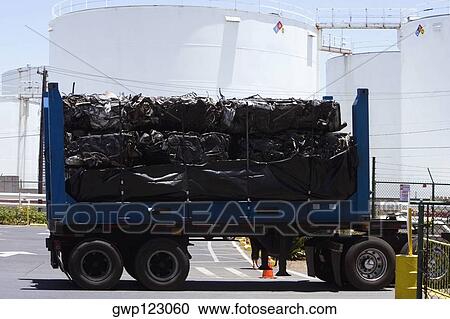 Stock Image - Vehicle trailer on the road with storage tanks in the background. Fotosearch
