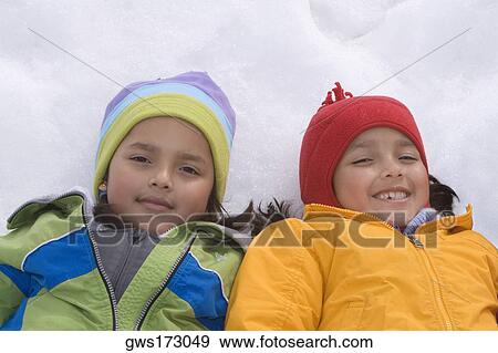 Stock Photo - High angle view of two girls lying in snow and smiling. Fotosearch