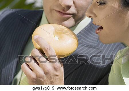 Stock Photo - Close-up of a businessman feeding donut to a businesswoman. Fotosearch