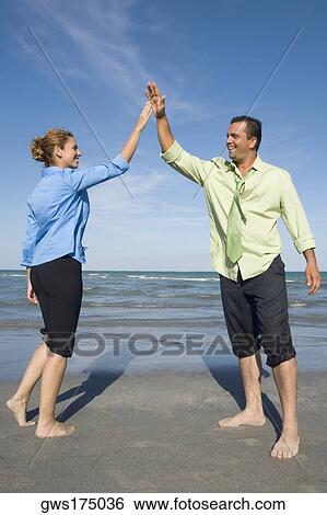 Stock Photograph - Mid adult couple giving high-five to each other and smiling. Fotosearch