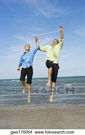 Mid adult couple jumping with holding each other hands on the beach View Large Photo Image Picture - Mid adult couple jumping with holding each other hands on the beach. Fotosearch