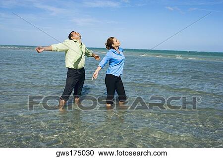 Mid adult couple standing on the beach with their arms outstretched View Large Photo Image Stock Image - Mid adult couple standing on the beach with their arms outstretched. Fotosearch