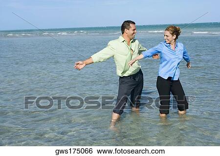 Mid adult couple standing on the beach with their arms outstretched View Large Photo Image Stock Photograph - Mid adult couple standing on the beach with their arms outstretched. Fotosearch