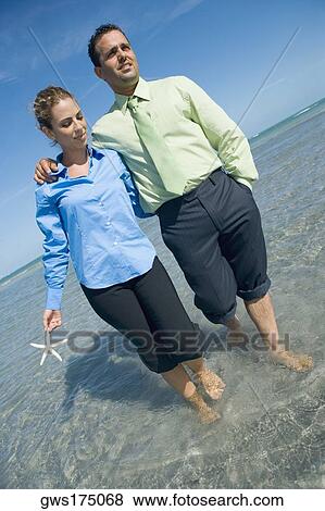 Mid adult couple wading on the beach with their arms around each other View Large Photo Image Stock Photo - Mid adult couple wading on the beach with their arms around each other. Fotosearch