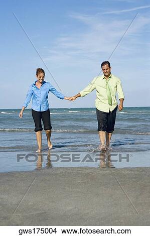 Mid adult couple walking on the beach with holding each others hands View Large Photo Image Picture - Mid adult couple walking on the beach with holding each others hands. Fotosearch