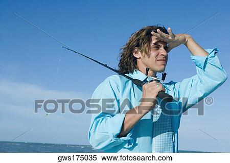 Mid adult man holding a fishing rod and looking away View Large Photo Image Stock Photography - Mid adult man holding a fishing rod and looking away. Fotosearch