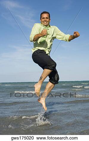 Stock Image - Mid adult man jumping on the beach. Fotosearch