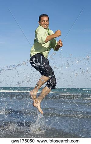 Stock Image - Mid adult man jumping on the beach. Fotosearch