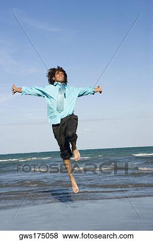 Mid adult man jumping on the beach with his arm outstretched View Large Photo Image Stock Photo - Mid adult man jumping on the beach with his arm outstretched. Fotosearch