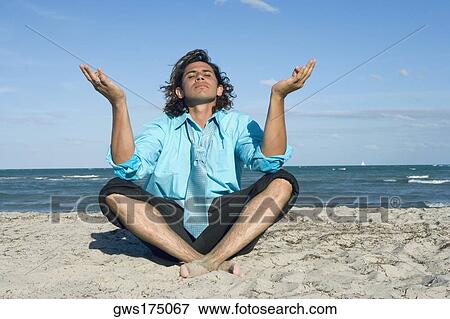 Stock Photo - Mid adult man meditating on the beach. Fotosearch