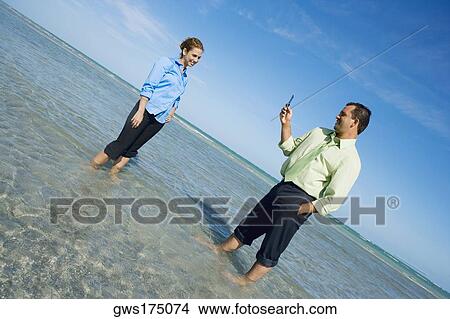Mid adult man taking a photograph of a mid adult woman on the beach View Large Photo Image Picture - Mid adult man taking a photograph of a mid adult woman on the beach. Fotosearch