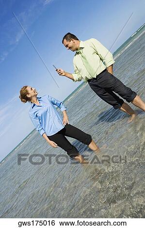 Mid adult man taking a photograph of a mid adult woman on the beach View Large Photo Image Stock Photograph - Mid adult man taking a photograph of a mid adult woman on the beach. Fotosearch
