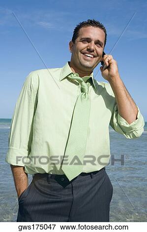 Stock Photo - Mid adult man talking on a mobile phone on the beach. Fotosearch