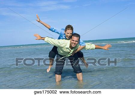 Mid adult woman riding piggyback on a mid adult man with their arms outstretched on the beach View Large Photo Image Stock Image - Mid adult woman riding piggyback on a mid adult man with their arms outstretched on the beach. Fotosearch
