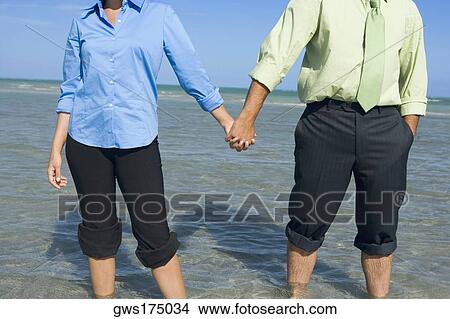 Mid section view of a mid adult couple standing on the beach with holding their hands View Large Photo Image Picture - Mid section view of a mid adult couple standing on the beach with holding their hands. Fotosearch