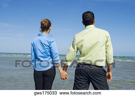 Rear view of a mid adult couple standing on the beach and holding hands View Large Photo Image Stock Image - Rear view of a mid adult couple standing on the beach and holding hands. Fotosearch