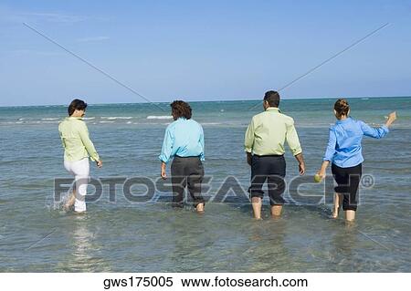 Stock Photography - Rear view of two mid adult couples wading on the beach. Fotosearch