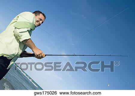 Side profile of a mid adult man holding a fishing rod on the beach View Large Photo Image Stock Photograph - Side profile of a mid adult man holding a fishing rod on the beach. Fotosearch