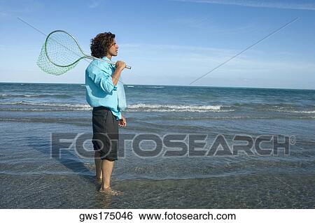 Side profile of a mid adult man holding a fishing net on the beach View Large Photo Image Stock Photograph - Side profile of a mid adult man holding a fishing net on the beach. Fotosearch