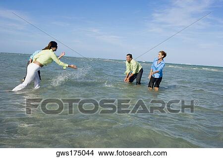 Side profile of two mid adult couples splashing water on each other on the beach View Large Photo Image Picture - Side profile of two mid adult couples splashing water on each other on the beach. Fotosearch