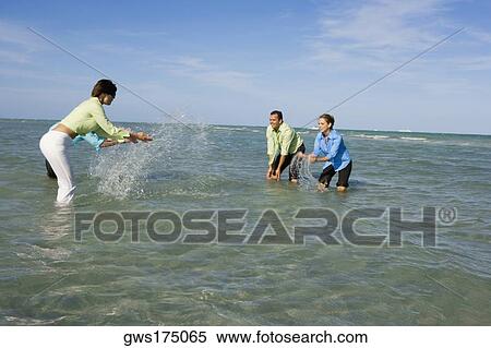 Stock Photography - Side profile of two mid adult couples splashing water on each other on the beach. Fotosearch