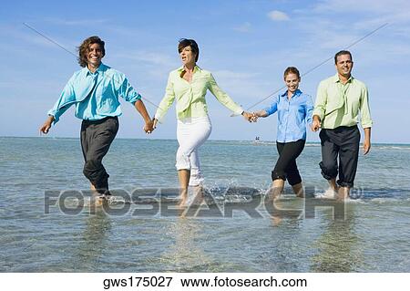 Two mid adult couples wading on the beach and holding hands of each other View Large Photo Image Stock Photo - Two mid adult couples wading on the beach and holding hands of each other. Fotosearch