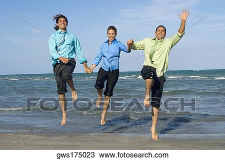 Two mid adult men with a mid adult woman holding each other's hands and jumping on the beach View Large Photo Image Stock Image - Two mid adult men with a mid adult woman holding each other's hands and jumping on the beach. Fotosearch