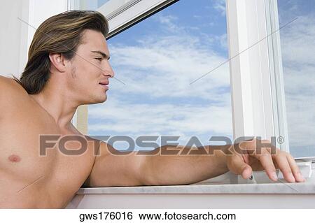 Close-up of a young man looking through a window View Large Photo Image Stock Photograph - Close-up of a young man looking through a window. Fotosearch