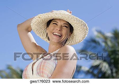 Mid adult woman wearing a straw hat and smiling View Large Photo Image Stock Image - Mid adult woman wearing a straw hat and smiling. Fotosearch