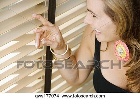 Picture - Close-up of a mature woman peeking through blinds. Fotosearch