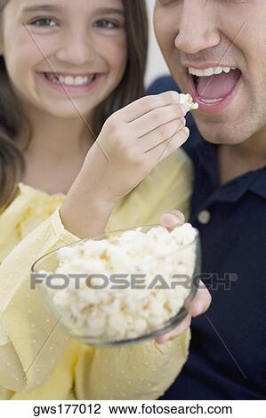 Portrait of a girl feeding popcorn to her father View Large Photo Image Stock Image - Portrait of a girl feeding popcorn to her father. Fotosearch