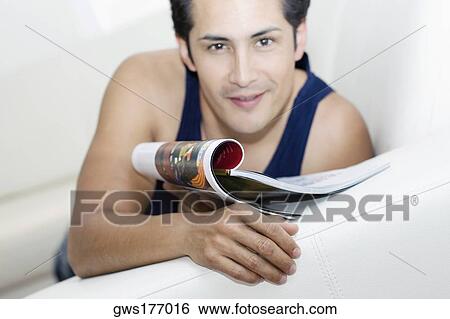 Portrait of a young man holding a magazine and smiling View Large Photo Image Stock Photograph - Portrait of a young man holding a magazine and smiling. Fotosearch