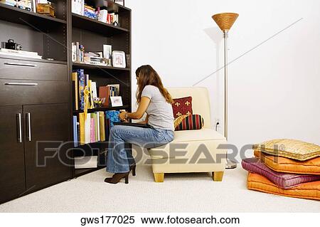Stock Photography - Side profile of a woman sitting on a chair in a living room. Fotosearch
