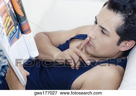 Stock Photo - Side profile of a young man reading a magazine with his finger on his lips. Fotosearch